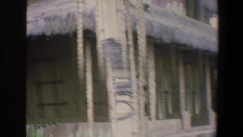 1973 Walt Disney World home-movie frame showing a closer view of tropical-themed building details, including a carved pillar, doorway, windows, roof edge, and plants.