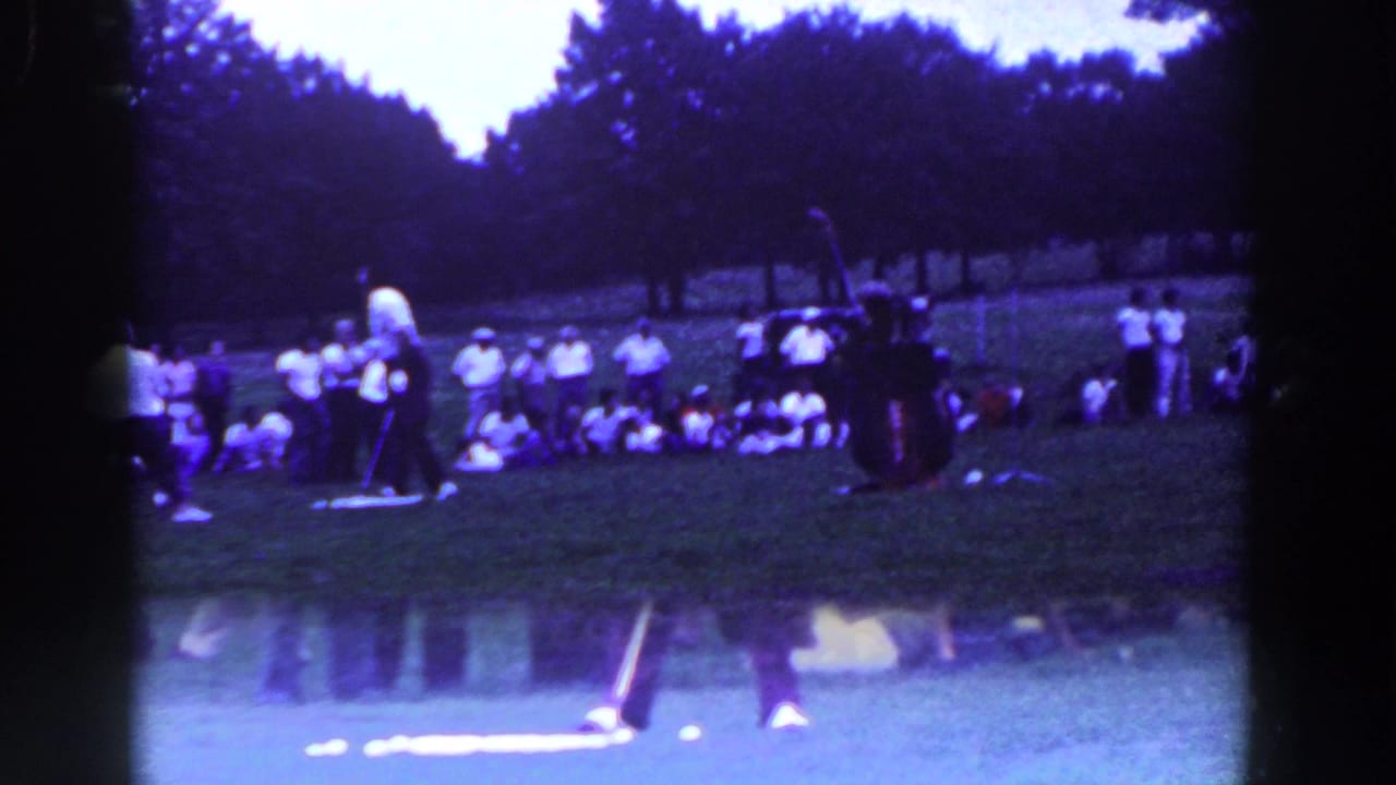 Wide golf-course view with spectators gathered near the grass and a club or marker in the foreground.