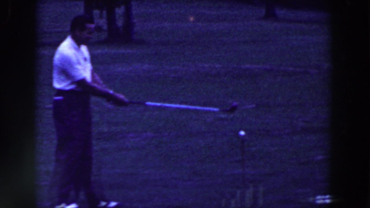 Man in a white polo shirt swings a golf club on a grassy course.
