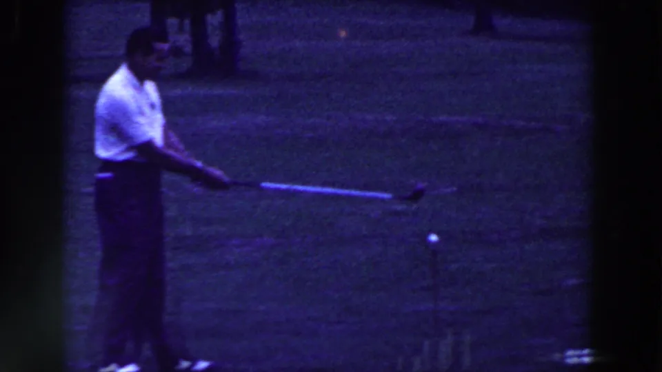 In 1961 Ridgefield, New Jersey home-movie footage, a man in a white polo swings a golf club on grass under a blue cast.