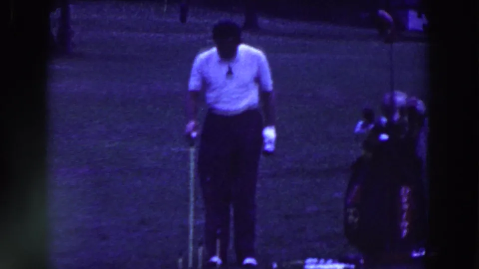 The golfer pauses with club in hand near a ball and golf bag, seen in blue-tinted 1961 Ridgefield home-movie footage.