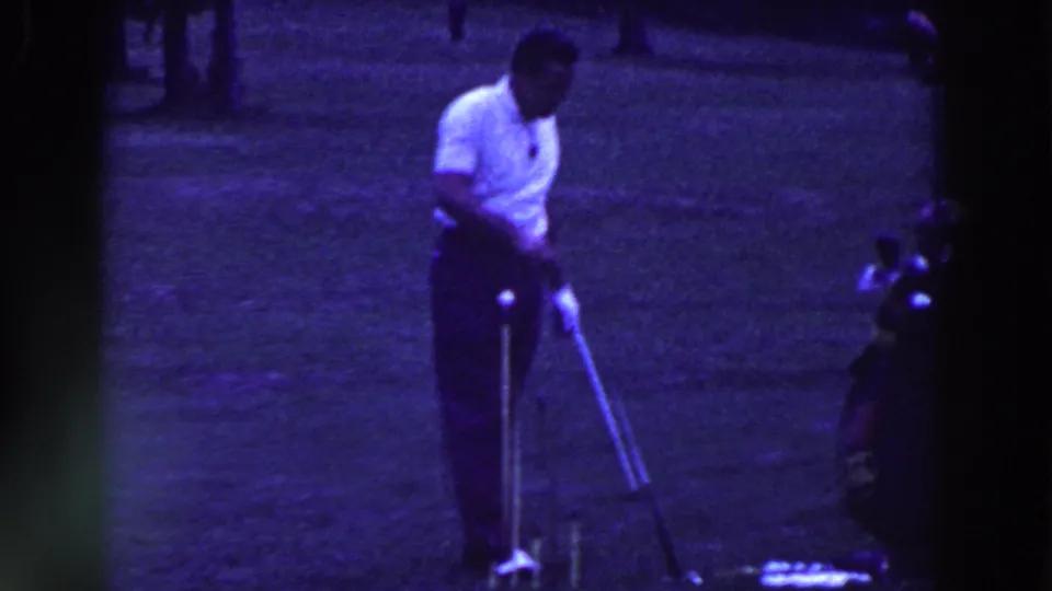 In Ridgefield, New Jersey in 1961, a man in a white shirt prepares a golf shot on a grassy course with trees behind him.
