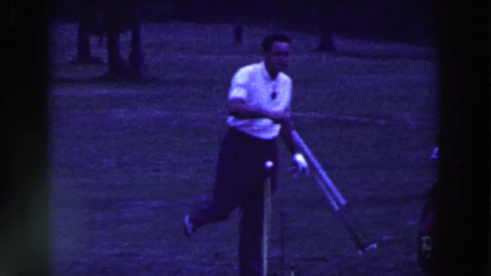 A male golfer in a white shirt swings on a grassy Ridgefield course, with a golf bag and trees visible in the 1961 home-movie frame.