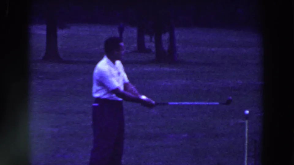 A man in a white shirt holds his golf club out after a swing on a Ridgefield, New Jersey course, with grass and trees in the 1961 frame.