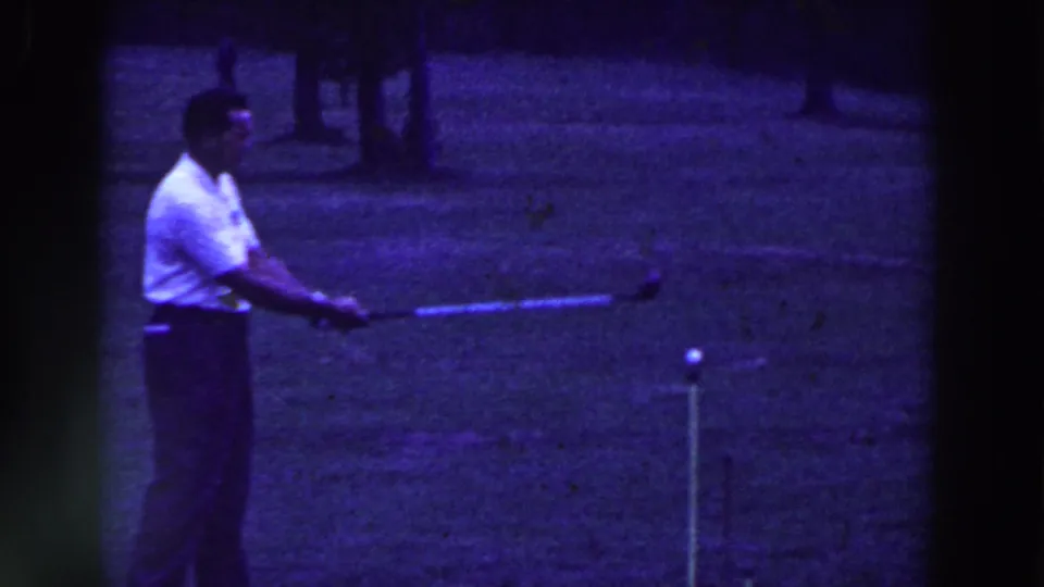 In 1961 Ridgefield, New Jersey home-movie footage, a man in a white shirt prepares to strike a golf ball on a grassy course.