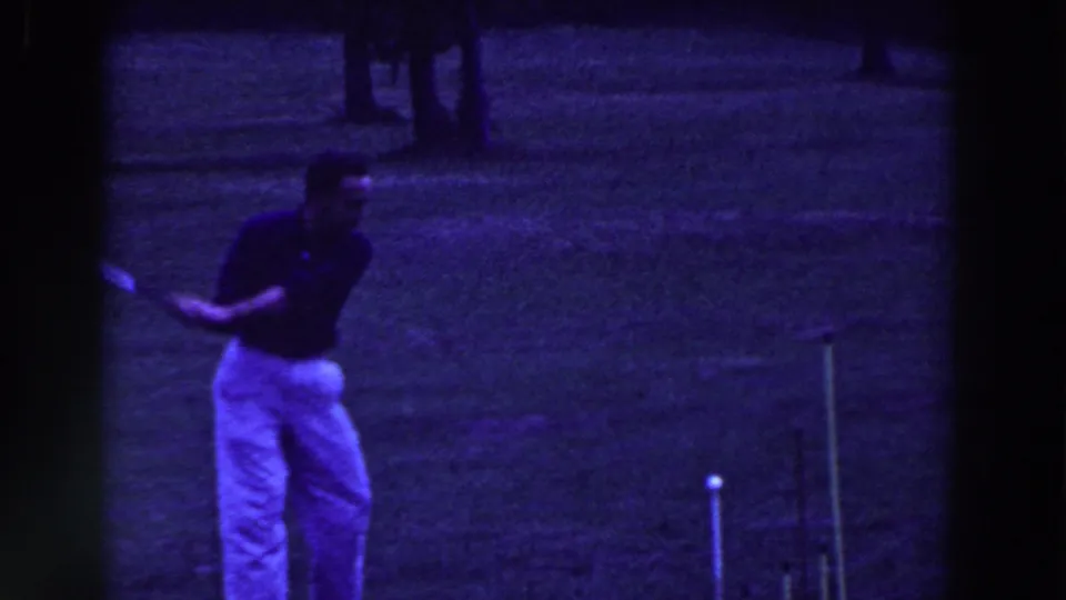 The man follows through with the croquet mallet on the lawn, with the ball and stakes visible in the frame.