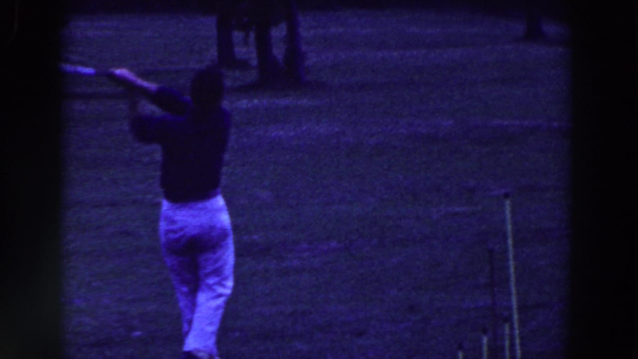 Golfer seen from behind finishing a swing on a dark grassy course.