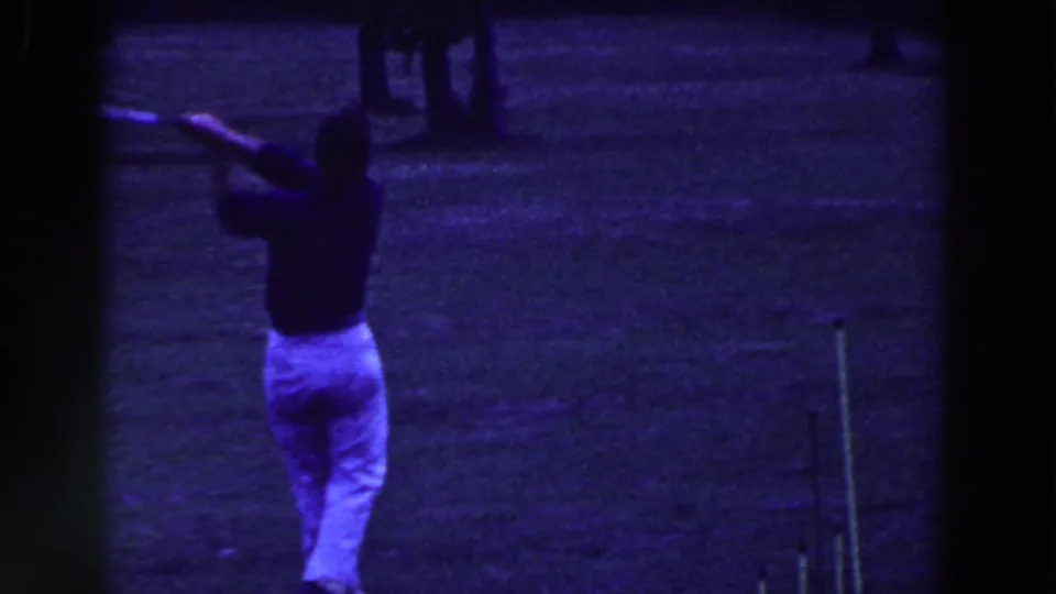 In 1961 Ridgefield, New Jersey footage, a golfer in light trousers and a dark shirt follows through on a grass course.