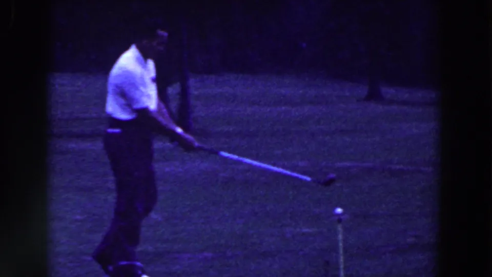 A golfer in a white short-sleeved shirt and dark pants prepares to strike a ball on a Ridgefield grass course in 1961.