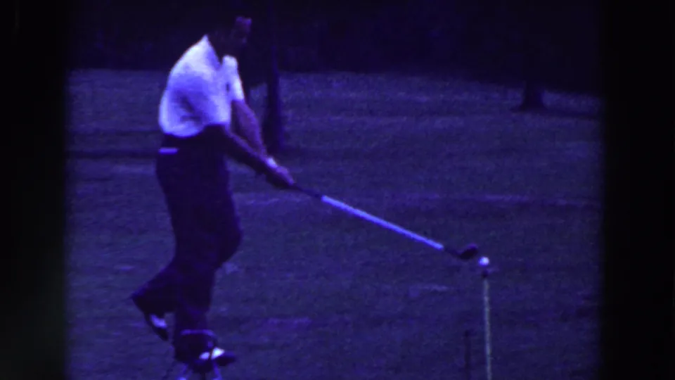 The 1961 Ridgefield home-movie frame shows the golfer moving through a low swing near a ball on the grass.