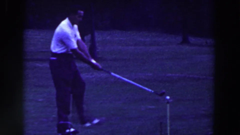 A golfer in white shirt and dark pants continues his swing on a Ridgefield, New Jersey course in the 1961 8mm footage.