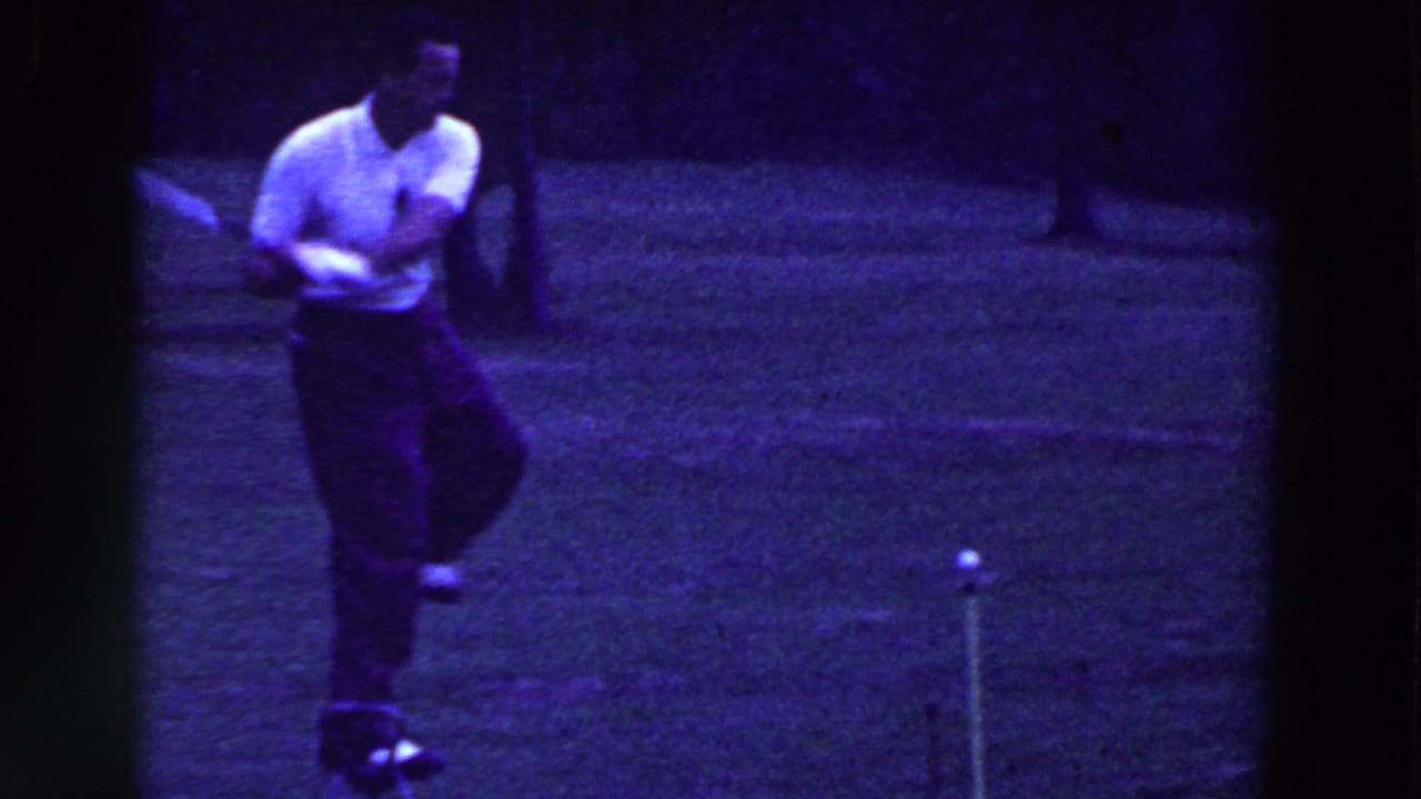 Man in white shirt stands on grass holding a golf club during a trick demonstration.