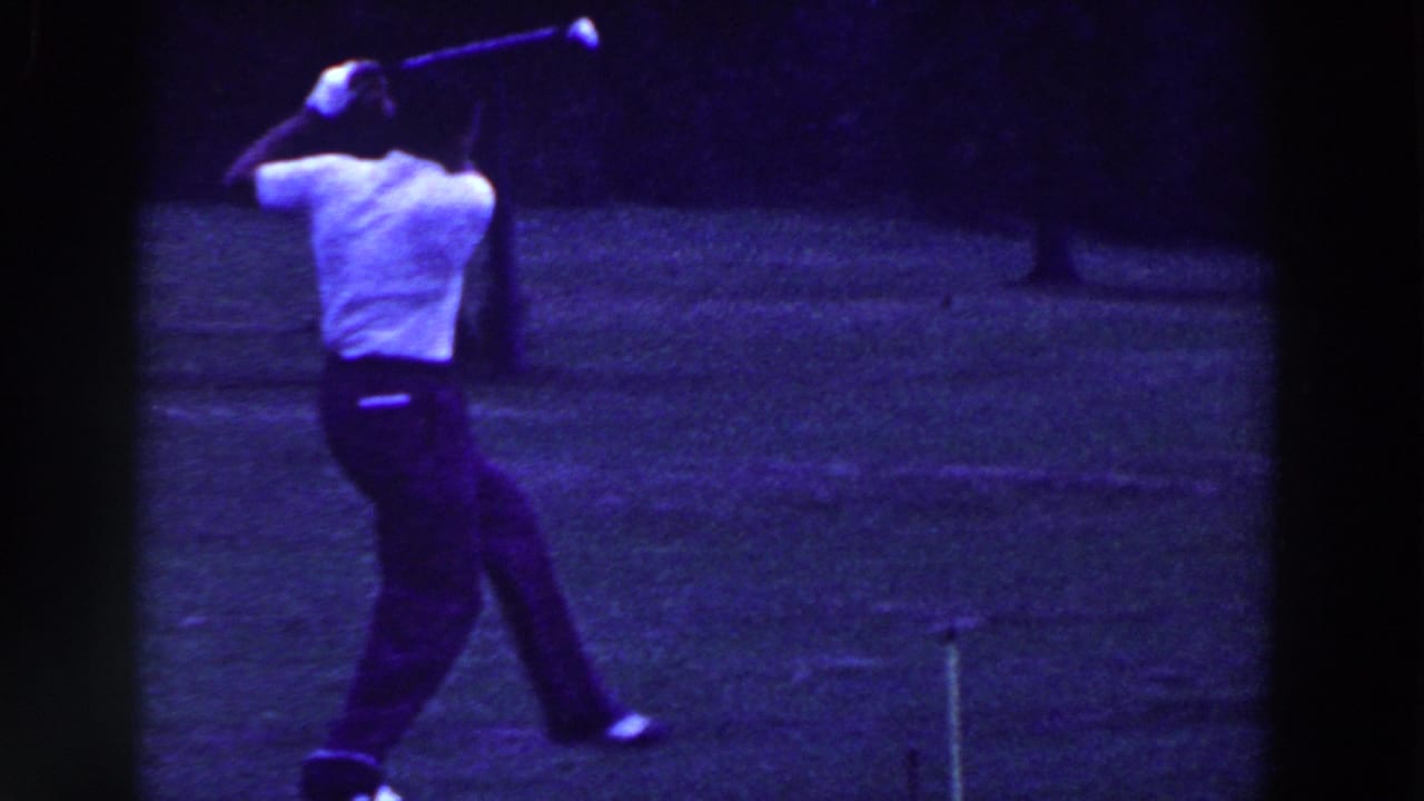 Man completes a golf swing with the club raised over his shoulder on grass.