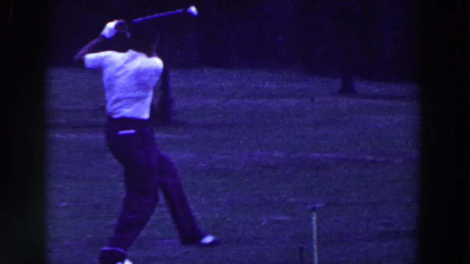 The golfer follows through with his club raised high, filmed in purple-blue 8mm color on a grassy course in Ridgefield, New Jersey.