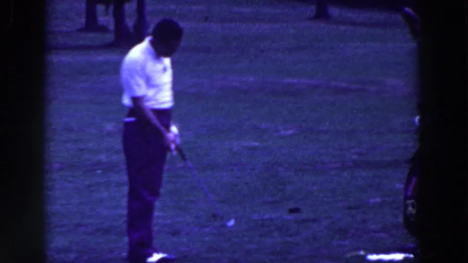 The golfer looks down toward the ground while holding his club on the Ridgefield course, with grass and trees behind him.