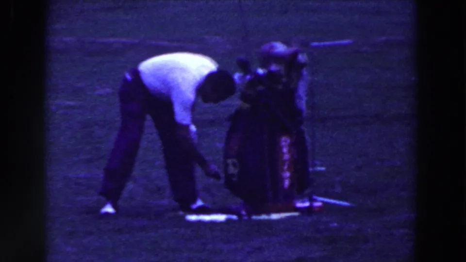 A man bends toward the ground beside a standing golf bag on the 1961 Ridgefield golf course.