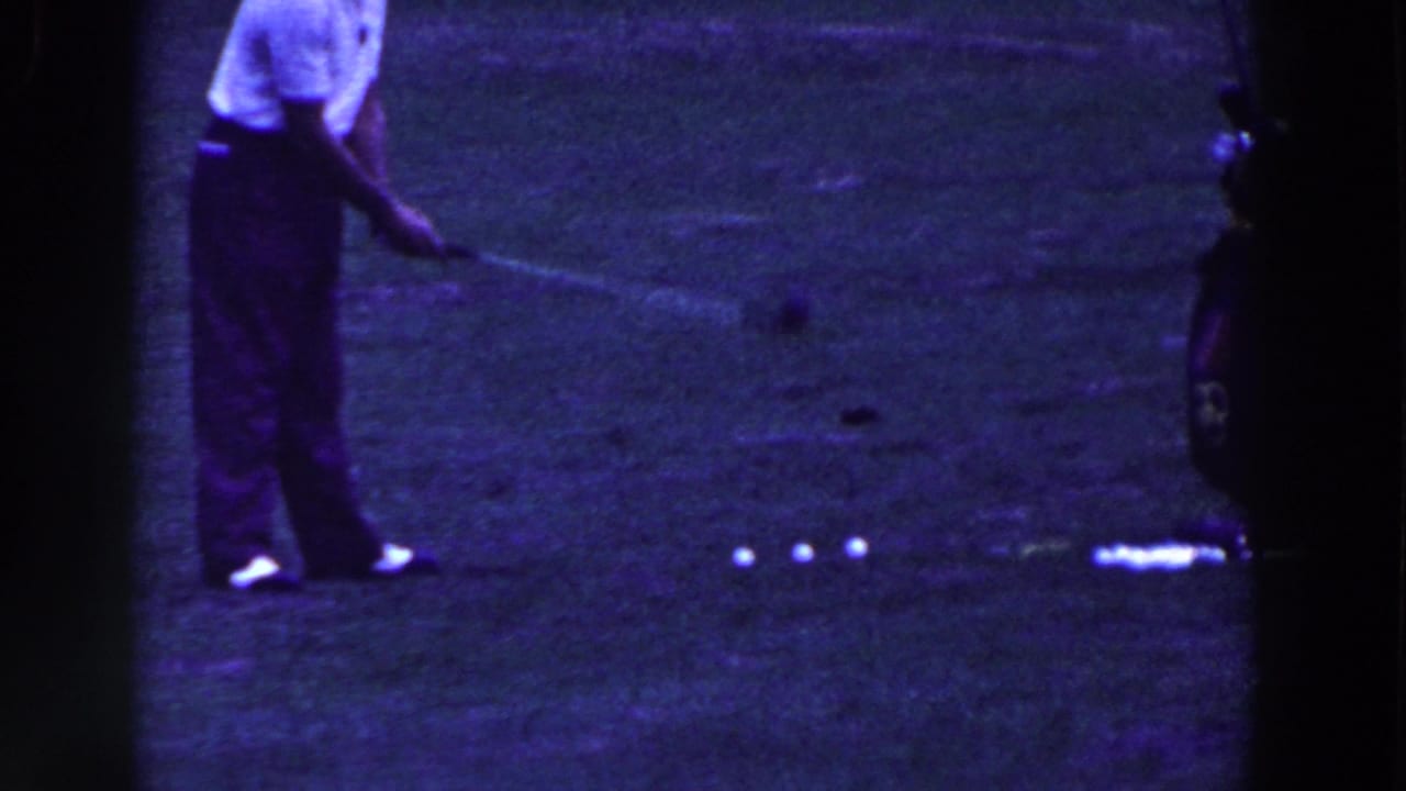 Man in white polo stands on grass near several white golf balls.