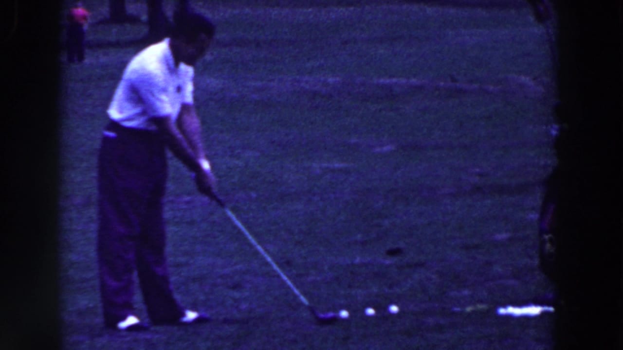 Golfer addresses a white ball with a club on a grassy course.