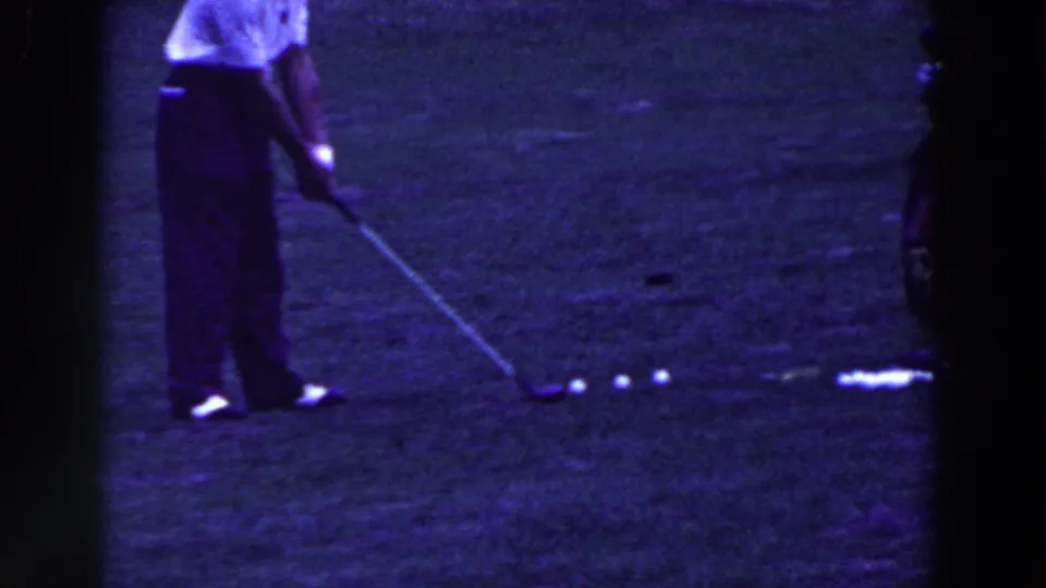 The golfer returns to an address position over a white ball, with a small line of golf balls nearby on the grassy course.