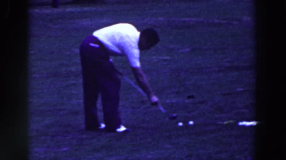 A man bends toward golf balls on a grassy course in 1961 Ridgefield, New Jersey home-movie footage.