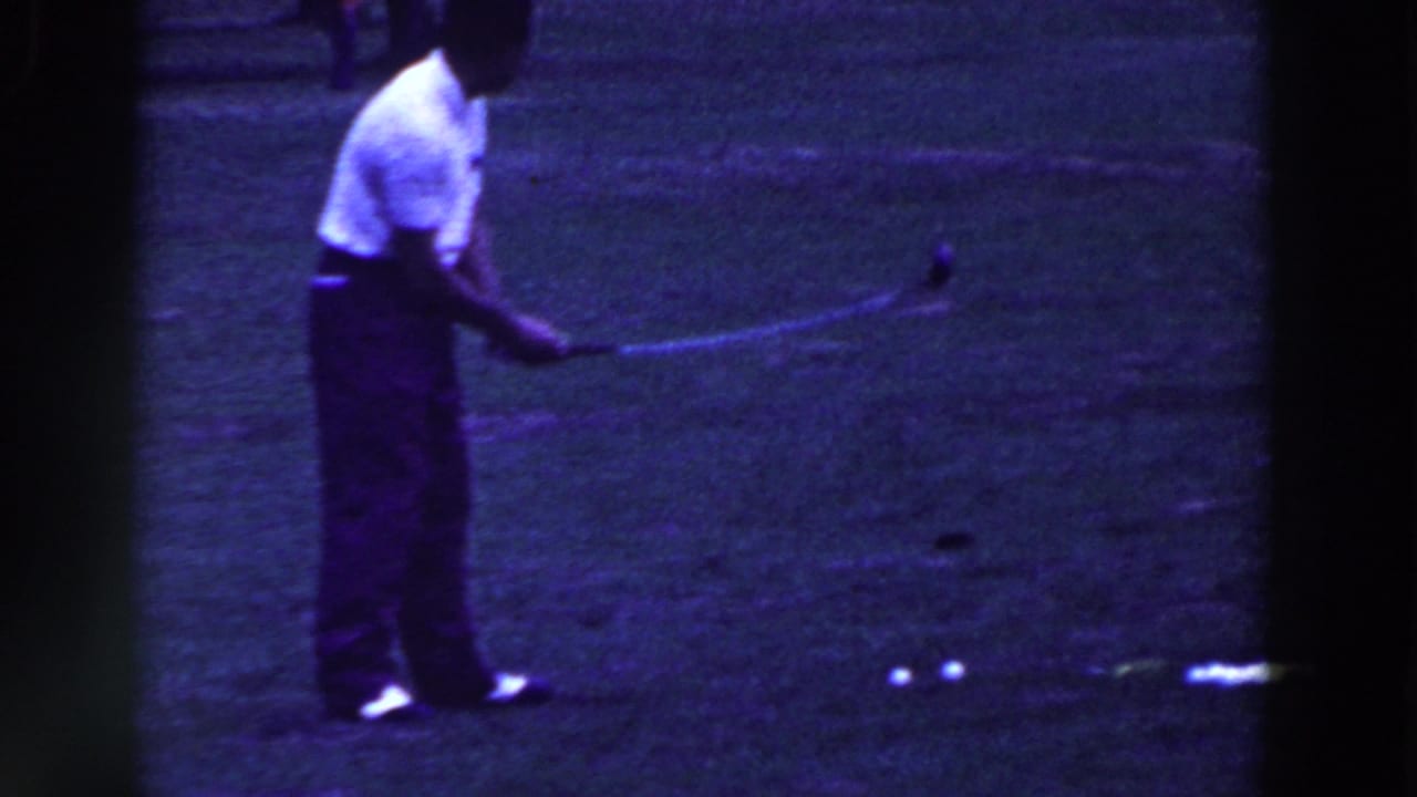Man holds a golf club near several balls on the grass.