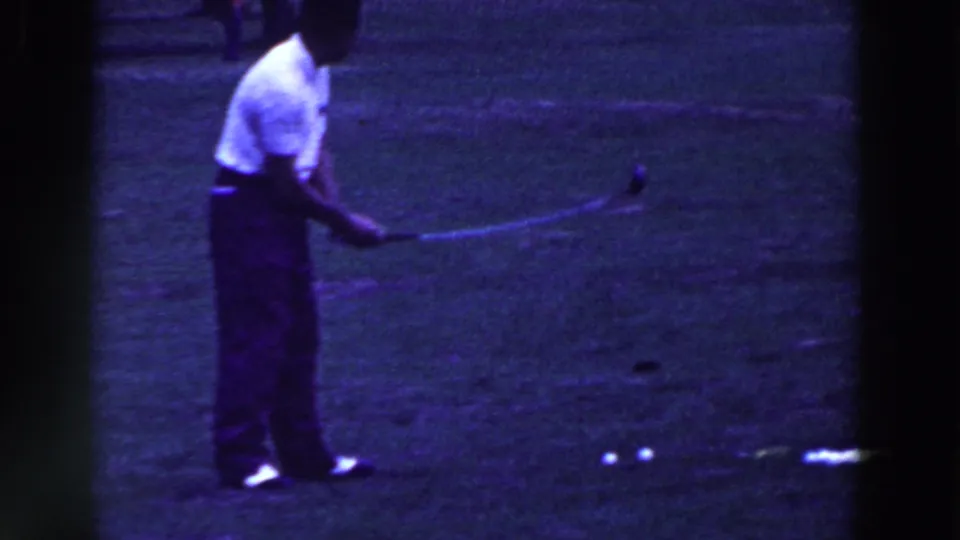 The golfer stands over the ball in the 1961 Ridgefield footage, with several white balls visible on the grass.