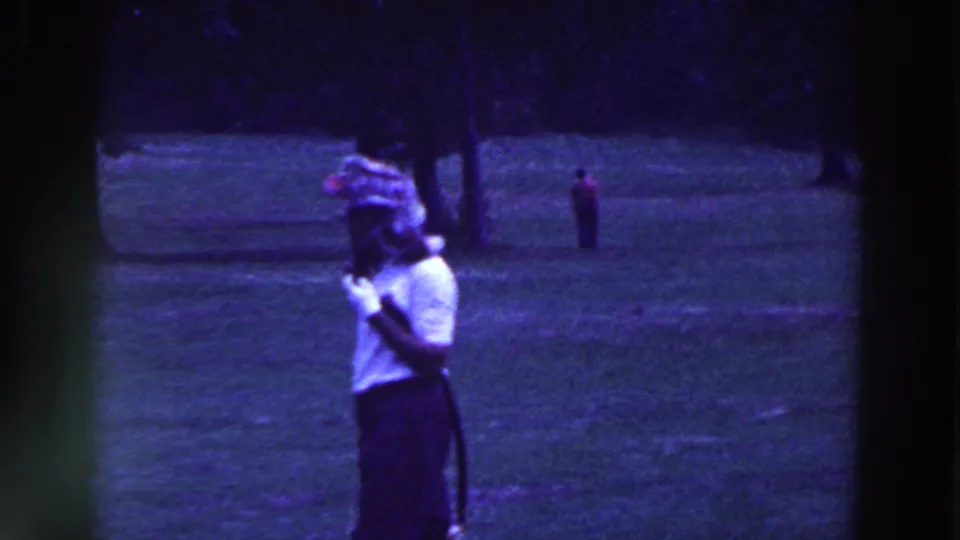 The woman pauses on the Ridgefield golf course, holding the club near her shoulder while a distant player stands on the fairway.