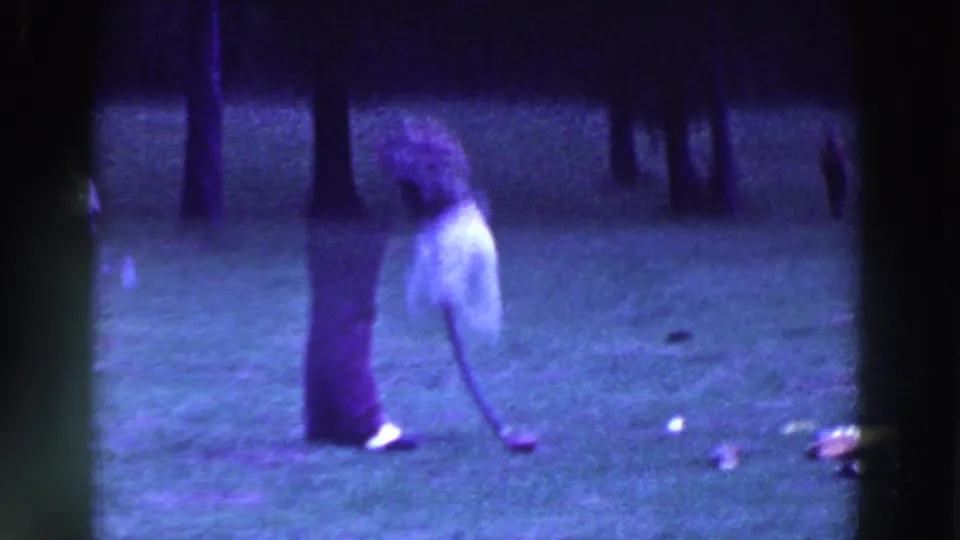 The woman bends toward the ball on the golf course, with the club lowered and the vintage 8mm frame softly exposed.