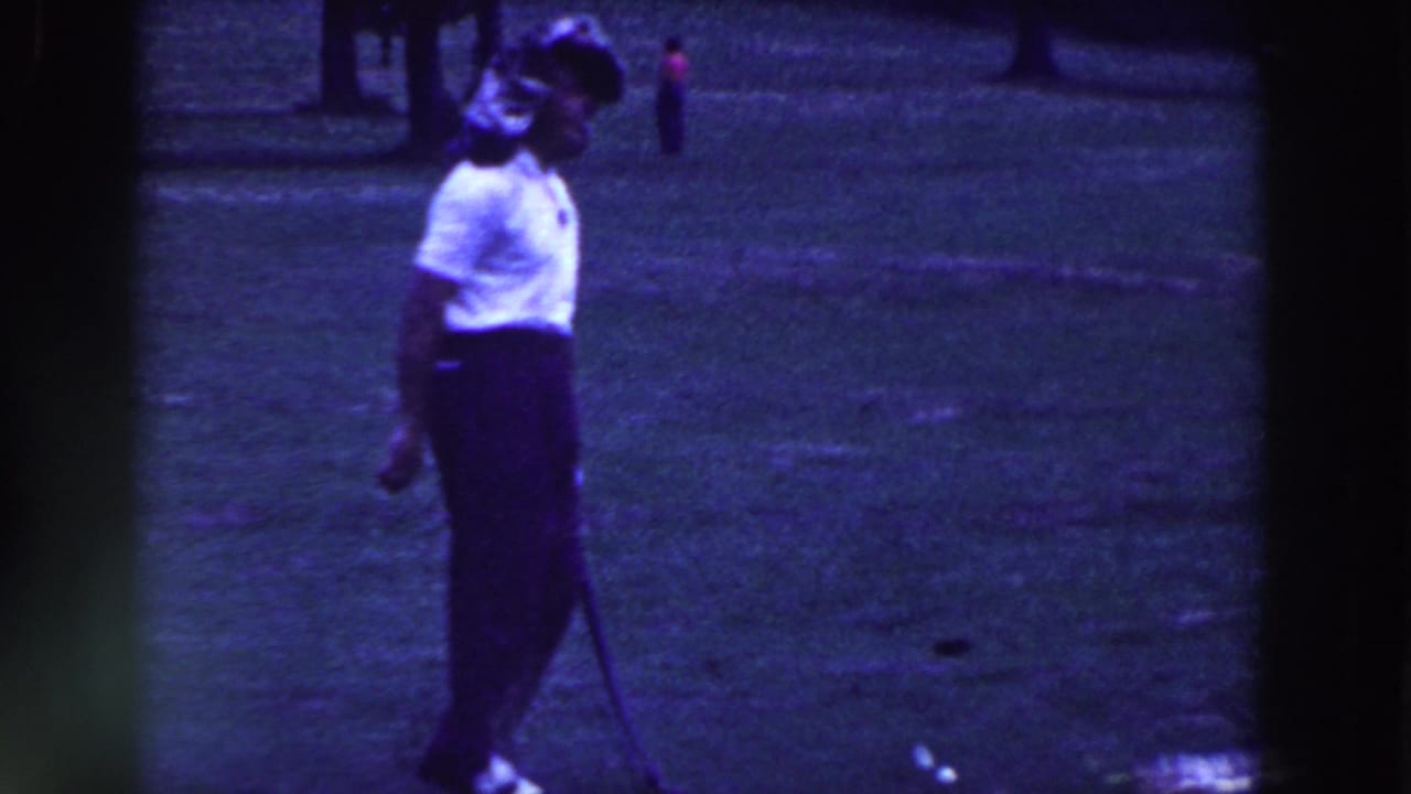 Man in a white shirt stands on grass holding a bent golf putter.
