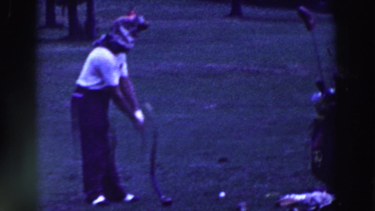 Man bends toward a golf ball with a curved putter on the grass.