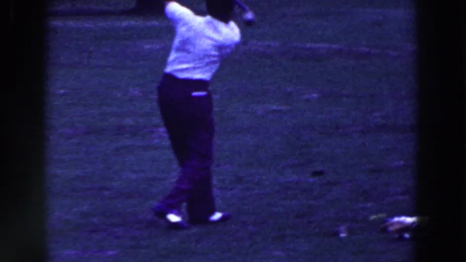 A man finishes his golf swing on an open grassy course, captured in purple-blue 8mm footage from 1961 Ridgefield, New Jersey.