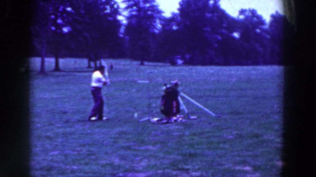 In 1961 Ridgefield, New Jersey, a man in a light shirt and dark trousers prepares a golf swing on an open grassy field.