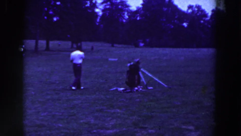 The golfer stands farther from the camera on the Ridgefield field, with a golf bag and club visible to one side.