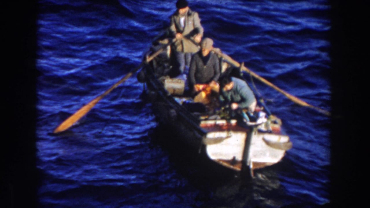 In this 1959 Gibraltar 8mm frame, three adult men occupy a small rowboat as long oars extend across rough blue water.