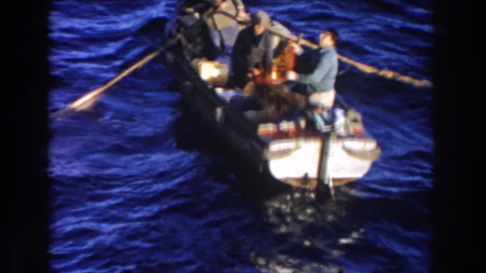 1959 Gibraltar home-movie frame showing a small boat with adults, oars, supplies, and choppy blue sea around it.