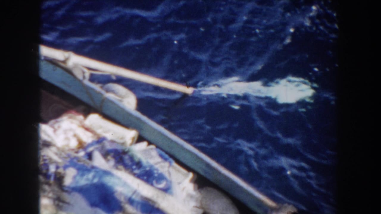 Small boat edge with bundled fabric beside dark blue ocean water and a paddle splash.