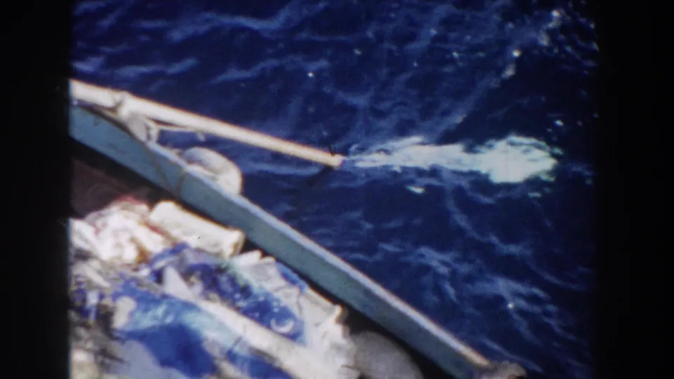 1959 Gibraltar home-movie frame showing a small boat edge, packed fabric, and a pale paddle splash on deep blue water.