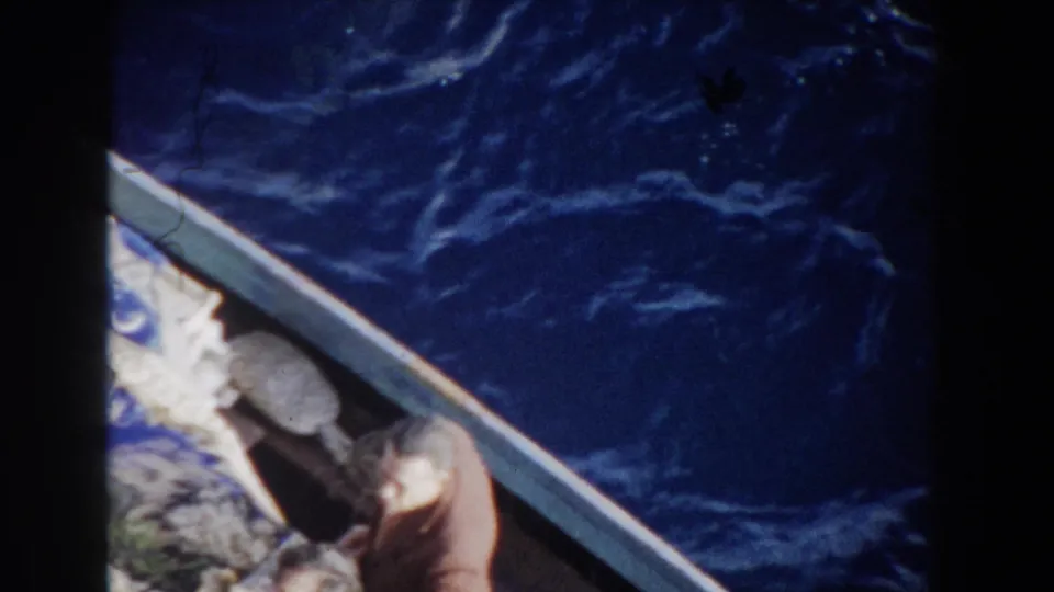 1959 Gibraltar home-movie view from above a small craft, showing blue water, packed items, and a partially visible adult passenger.