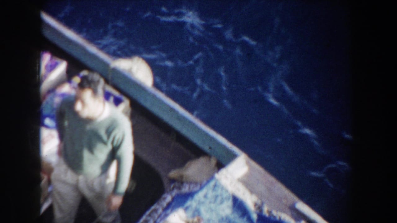 Adult man aboard a boat in 1959 Gibraltar travel footage, seen near the rail with dark sea beside him.