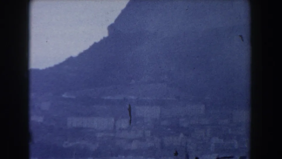 A handheld 1959 Gibraltar view shows the rocky slope and low coastal buildings through grain and haze.