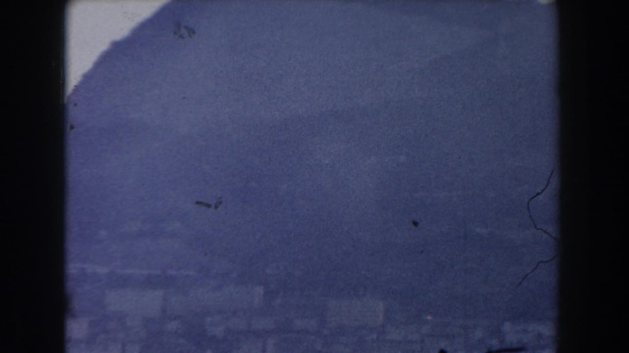 Hazy dark mountain slope beneath a pale sky with film borders and dust marks.