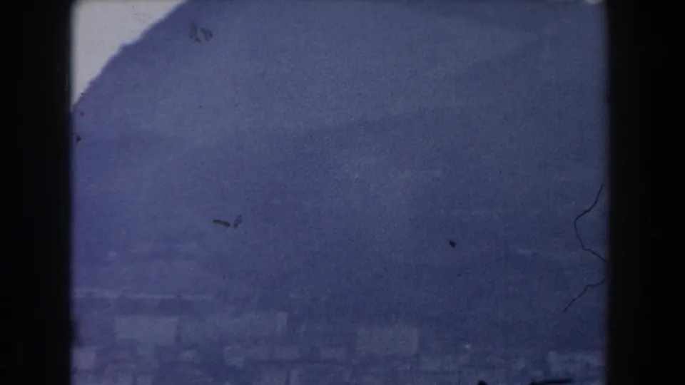 1959 Gibraltar 8mm frame showing a hazy dark mountain or rock face under a pale sky, with visible film grain and gate edges.