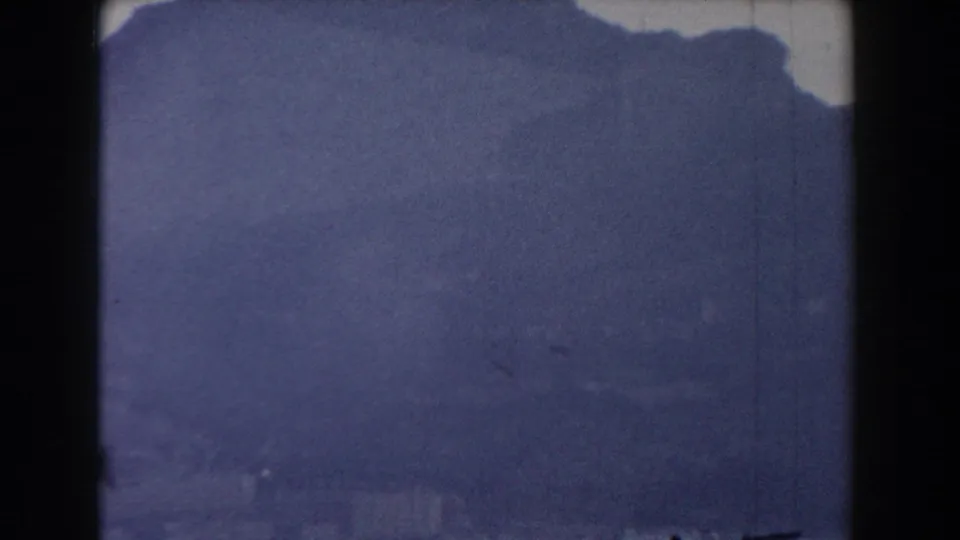 1959 Gibraltar 8mm frame with a subdued ridge silhouette, pale sky, grain, scratches, and a dark film divider at the left edge.