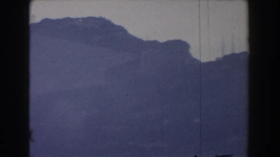1959 Gibraltar 8mm frame showing a rocky ridge line under pale sky, with soft focus, visible grain, and vertical scratch marks.