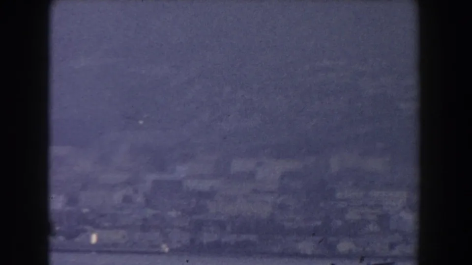 Grainy 8mm view over Gibraltar's hazy coastal buildings, with muted water visible along the lower frame.