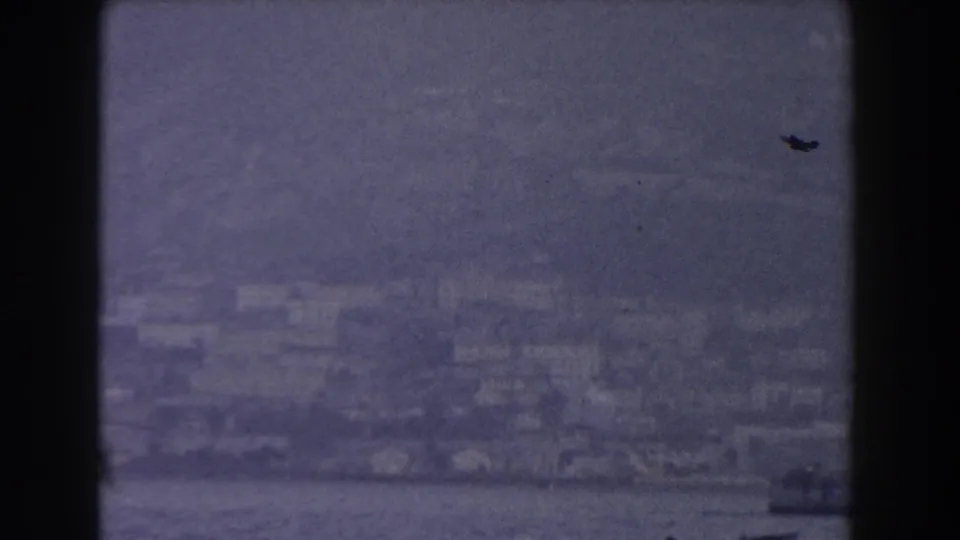 Blurred 1959 Gibraltar coastal city view with water at the bottom, haze over buildings, and dark 8mm frame edges.