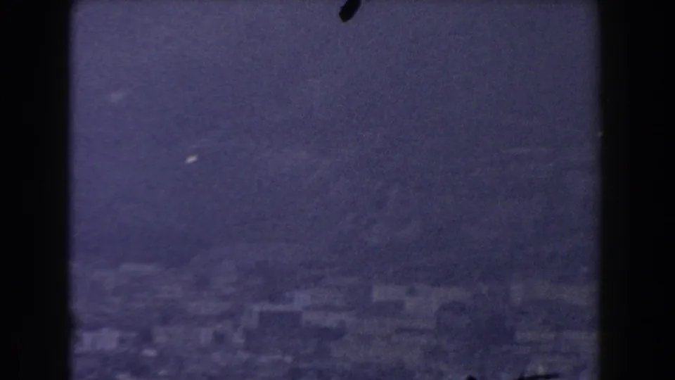 1959 Gibraltar home-movie view of a hazy shoreline with pale buildings below steep mountain terrain across the water.