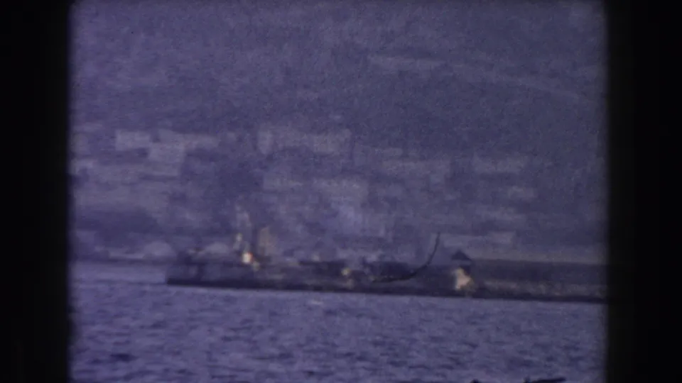The 8mm frame shows a ship in the foreground water with Gibraltar's hazy shoreline and hillside buildings beyond.