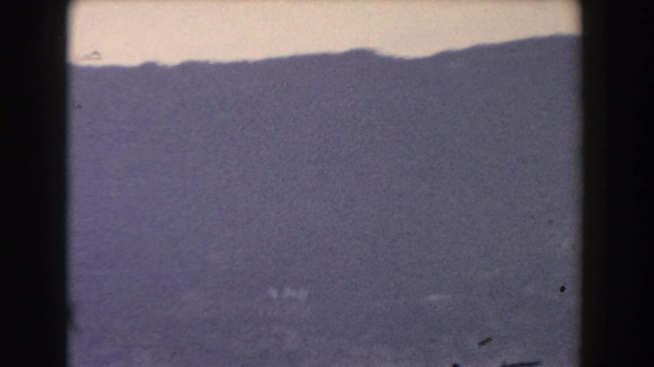 1959 Gibraltar 8mm frame showing a hazy dark mountain silhouette beneath a muted sky, with grain and film gate edges visible.