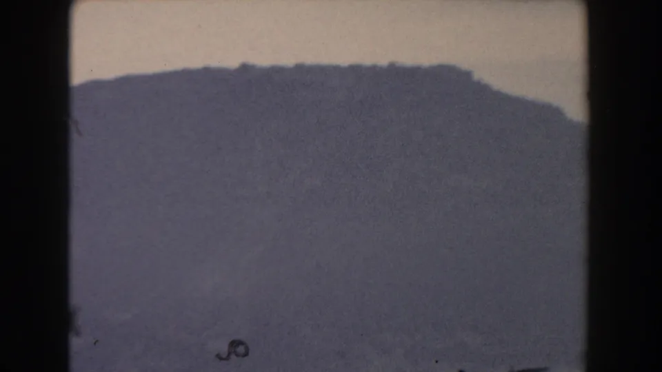 1959 Gibraltar home-movie frame with a broad grey mountain mass fading into mist under a washed, pale horizon.